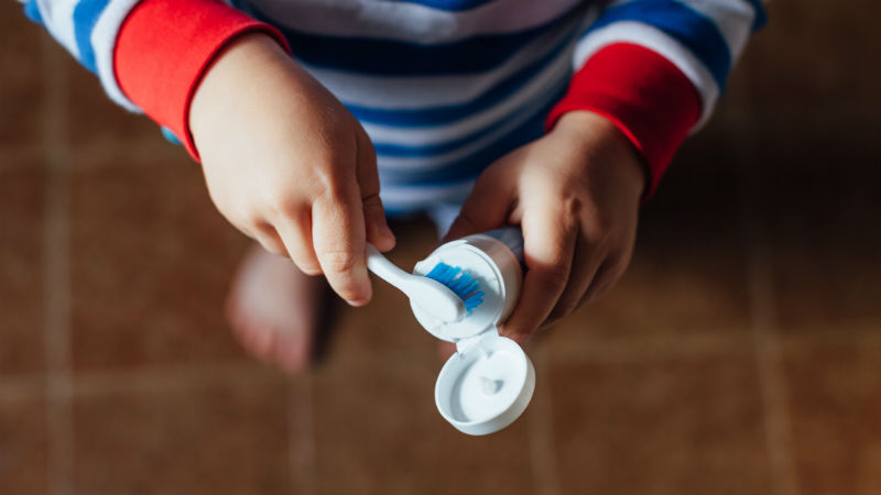 Child putting toothpaste on a toothbrush